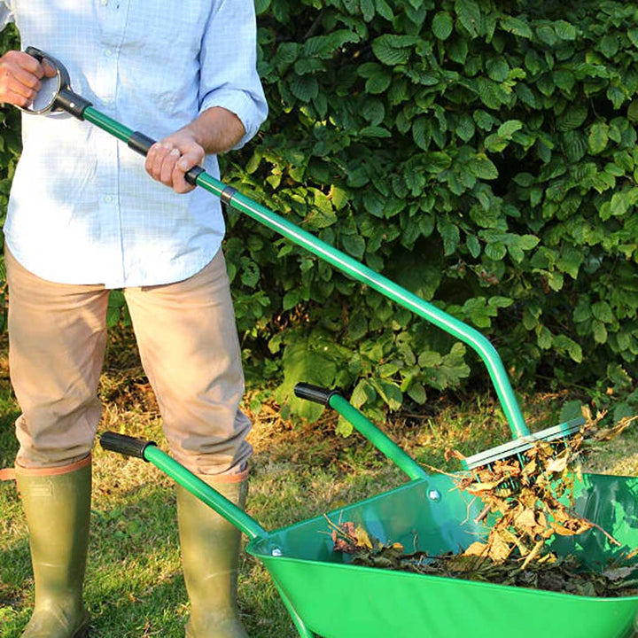 A person using a green leaf picker to collect leaves from a garden.